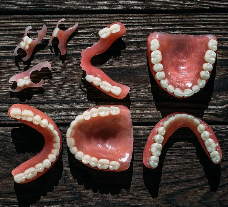 Dental prosthetics and denture models displayed on dark wooden surface, showing various teeth arrangements and configurations.