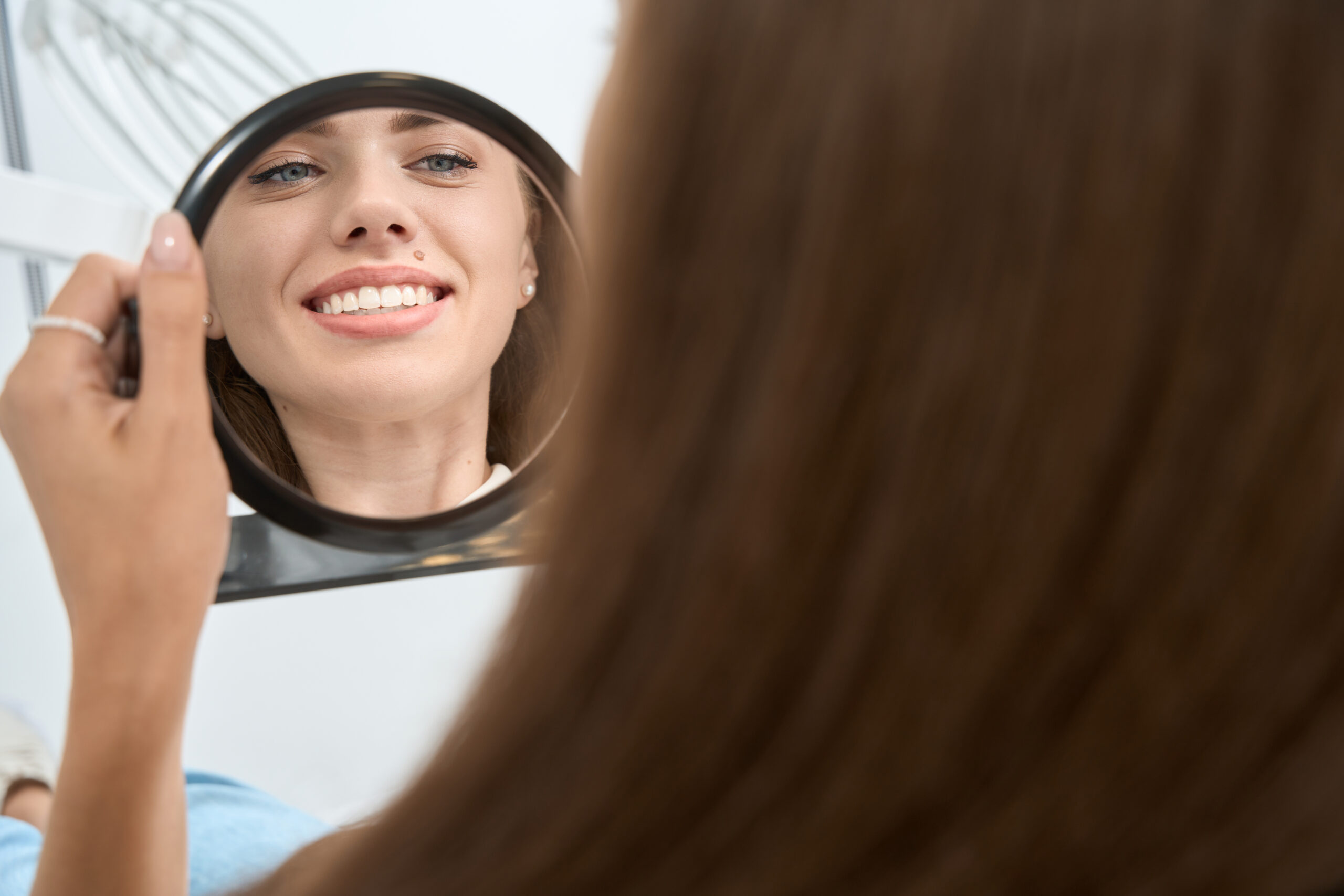 Patient smiling while examining her teeth in a mirror during a cosmetic dental visit