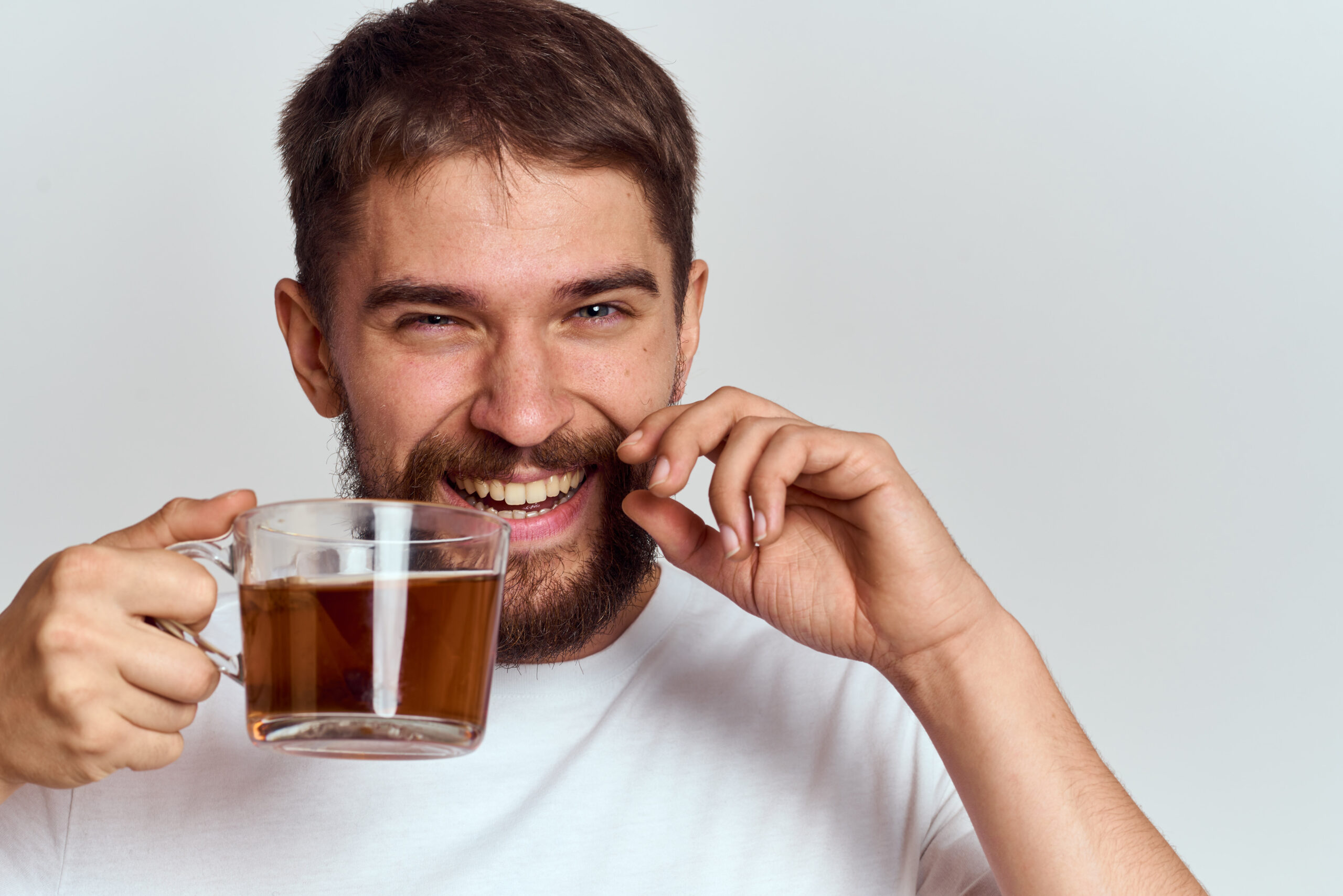 Smiling man holding a clear glass cup of tea, highlighting how coffee and tea can stain teeth over time.