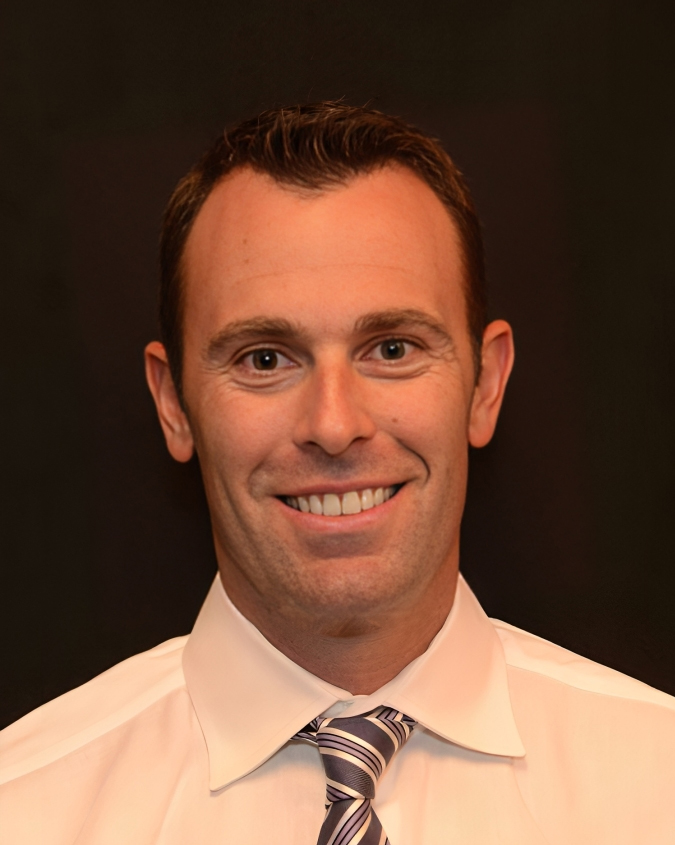 Professional headshot of Dr. Kevin R. Sambuchino, cosmetic dentist in Erie, PA, smiling against a dark background.