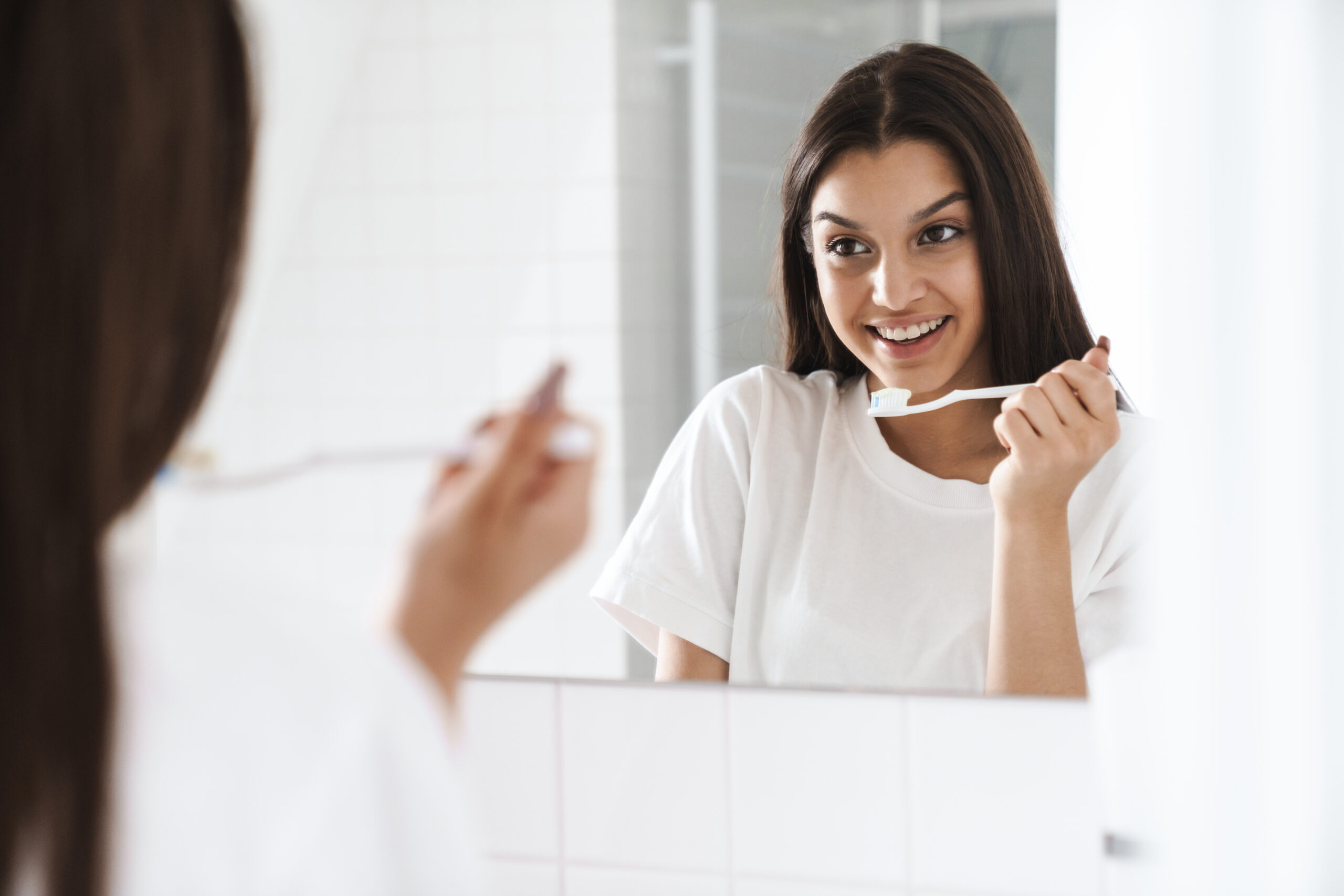 Woman brushing her teeth while looking in the mirror during her morning oral care routine.