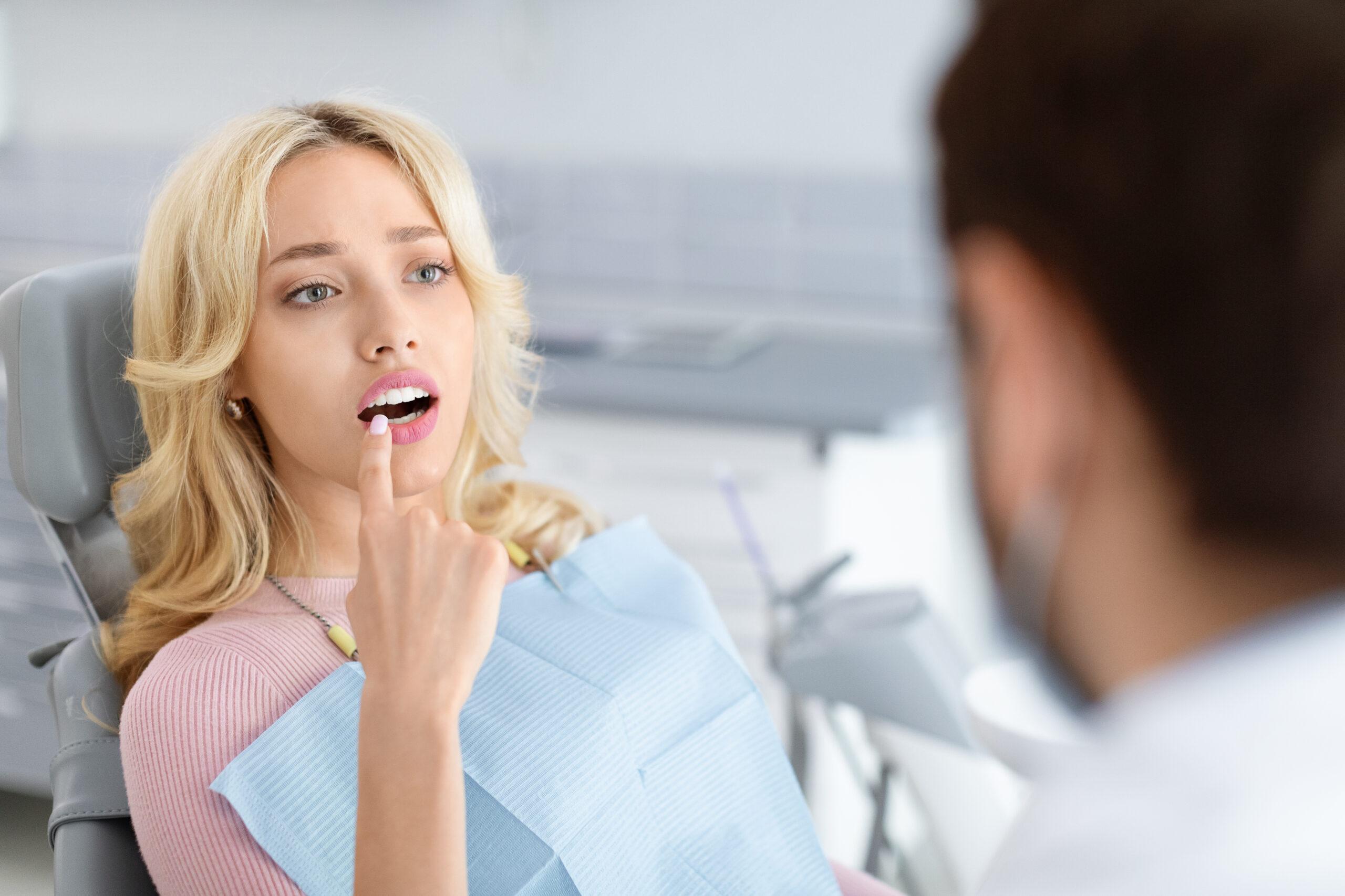 Patient pointing to worn front tooth while discussing cosmetic concerns with dentist during consultation